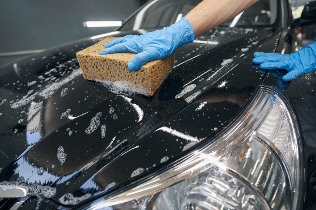 Car detailer washing black vehicle with sponge